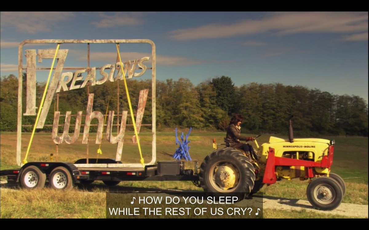 Bette is driving an enormous yellow tractor, with a trailer attached carrying the "17 reasons why!" billboard that they stole. Music plays in the background, singing, "How do you sleep while the rest of us cry?"