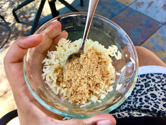 a brown hands holds a small bowl of coconut rice covered in a heavy sprinkle of gunpowder on top