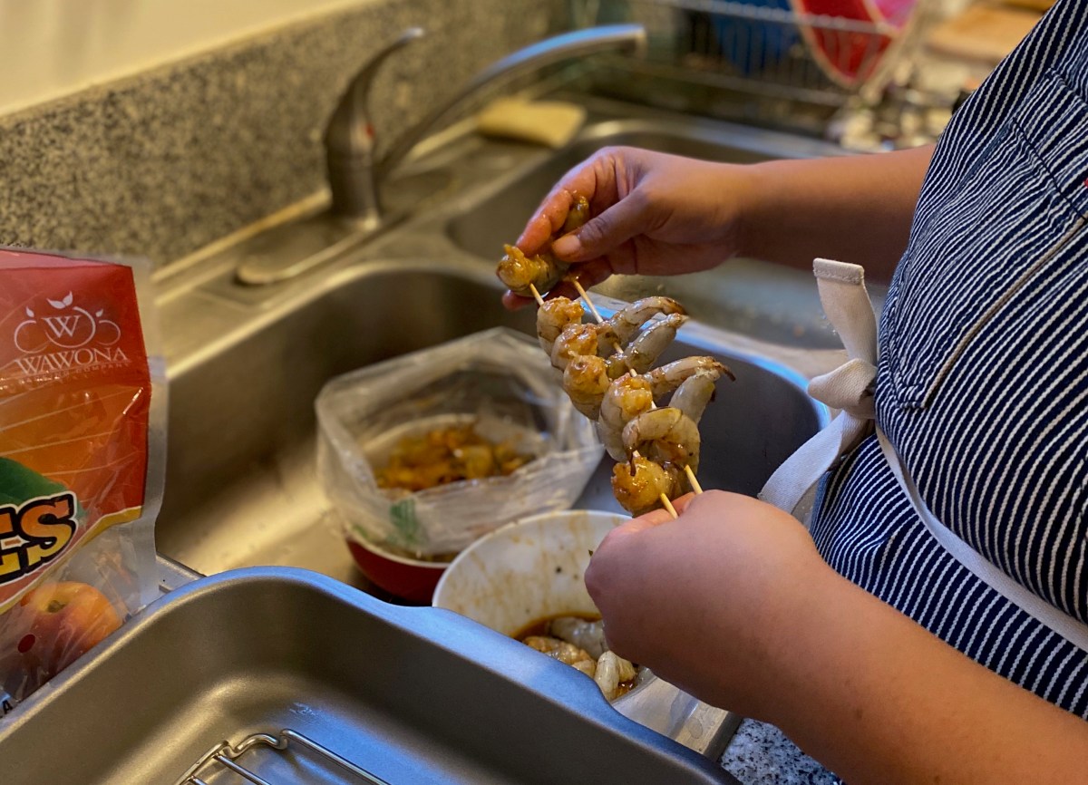 hands putting shrimp on skewers for grilling