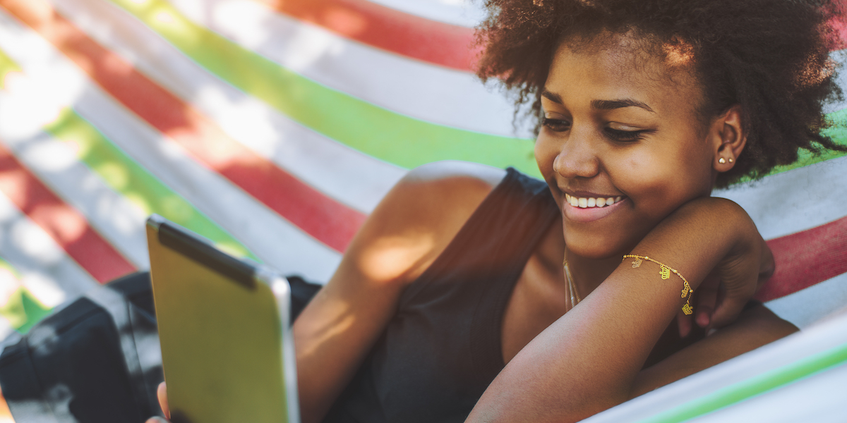 a woman with natural hair reading an ereader in a hammock