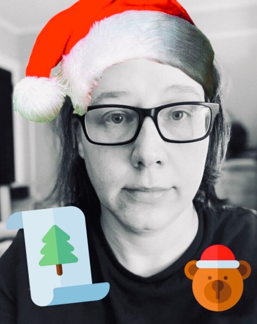 A Black and White photograph of Heather Hogan, with a bright red Santa hat photoshopped onto her head in the style of emoji animation.