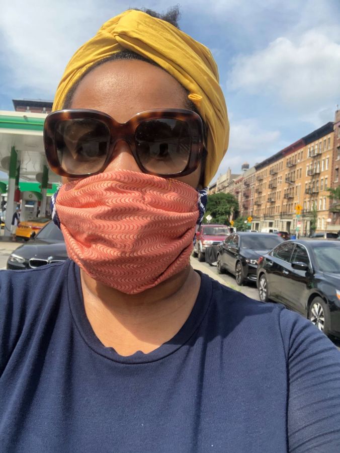 Jehan living New York city on moving day, she has a orange face bask and dark sunglasses and a yellow head wrap.