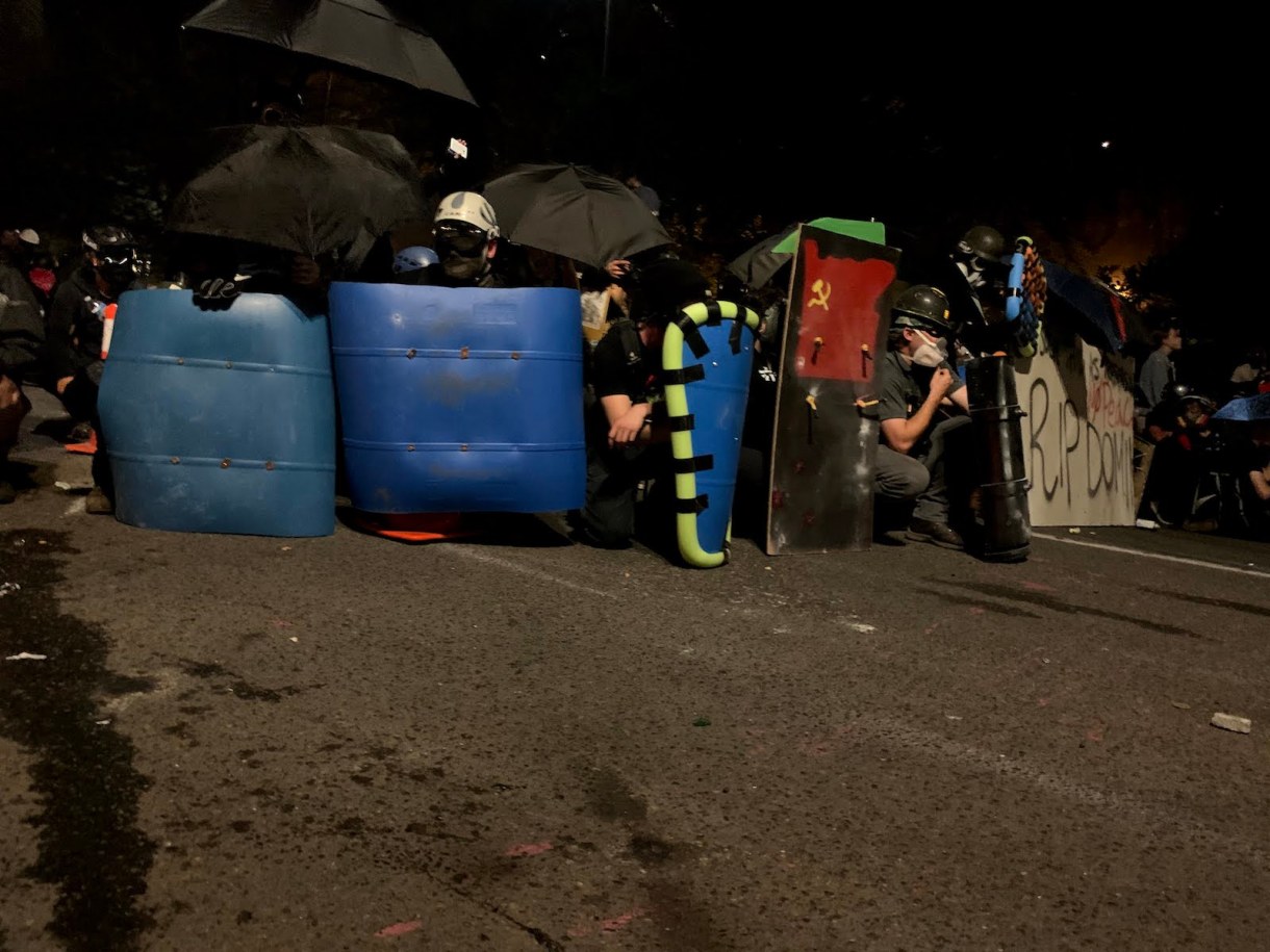 Protesters work together to create a protective shield line, holding their ground as federal officers fire pepper balls in their direction on July 21.