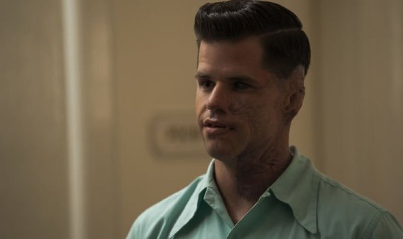 Charlie Carver as Huck in the Netflix show "Ratched." He stares off to the left in a light blue colored shirt and has brunette hair in a close cut style of the 1940s.