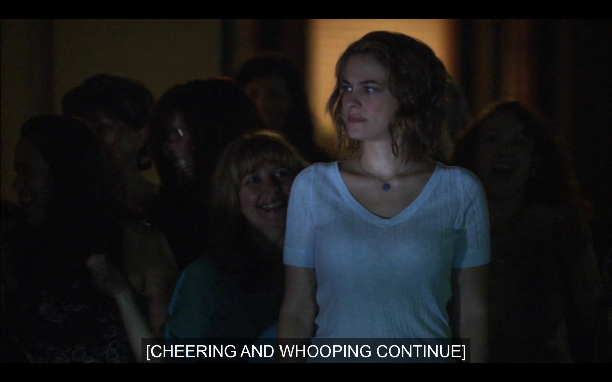 Molly is confused, standing at her mother's party in a white v-neck not sure what's going on. The caption reads "Cheering and whooping continue"