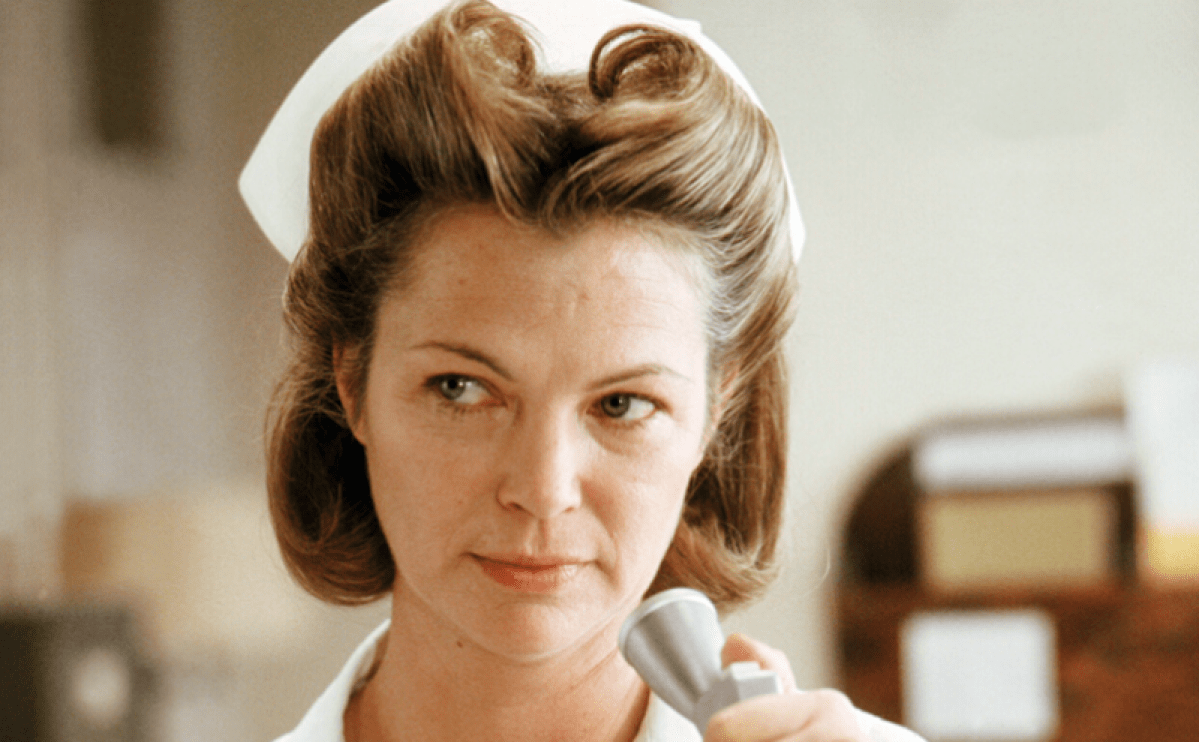 American actress Louise Fletcher as Nurse Ratched in 'One Flew Over The Cuckoo's Nest', directed by Milos Forman, 1975. She stares off to the right of the camera while speaking into a microphone.