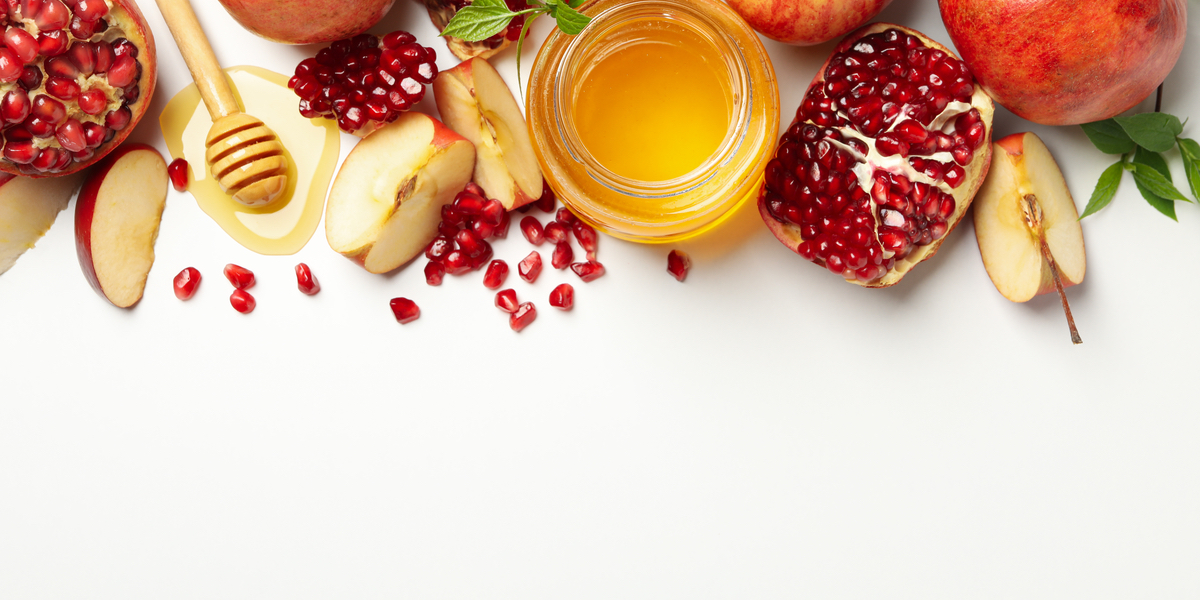 Rosh Hashanah theme on a white background including apples, honey, and pomegranates to symbolize the Jewish New Year