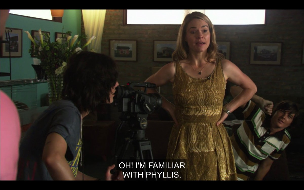 Alice in a gold lame dress at The Planet, hands on hips, saying "Oh, I'm familiar with Phyllis"