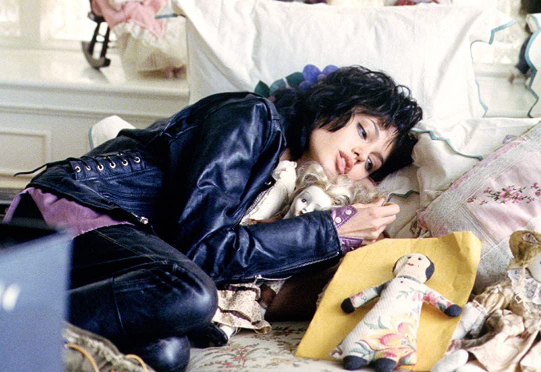 still of angelina jolie playing Gia in "Gia", wearing a leather jacket and looking longingly at some dolls