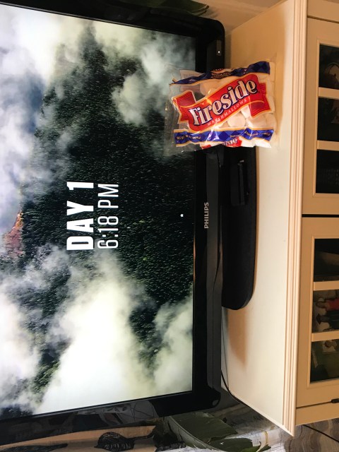 A bag of marshmallows propped up against a tv screen showing an outdoors reality show.