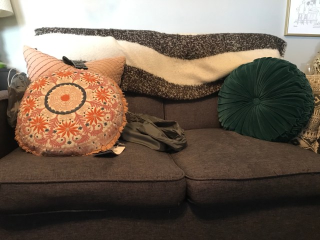 A brown couch with a blanket and a few throw pillows.