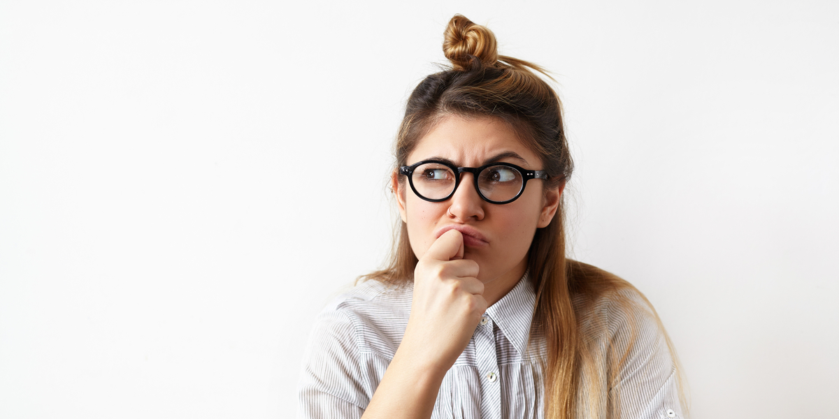 A woman wearing glasses holds her fist to her chin and raises one eyebrow