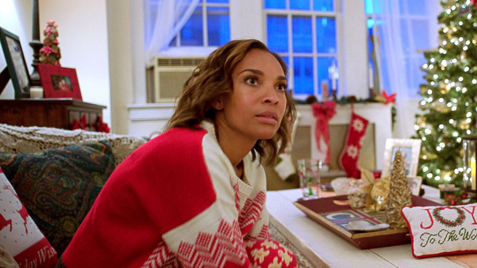 a woman in a red christmas sweater leans over a table covered with christmas decorations with a shocked and bereft look on her face