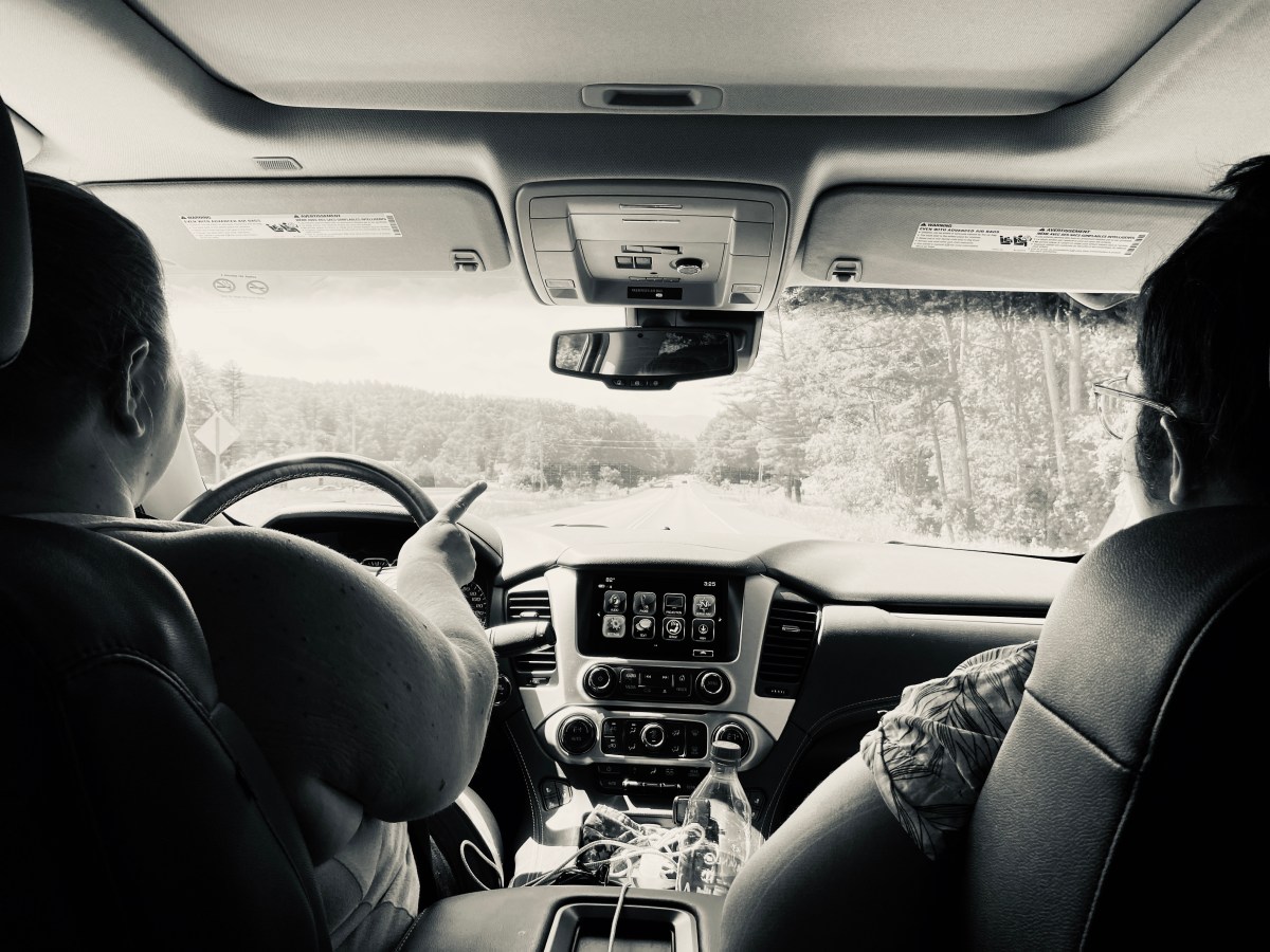 shot of the interior of a car from the backseat toward the windshield. two people are visible in the front seats and the person in the driver's seat is turning the steering wheel