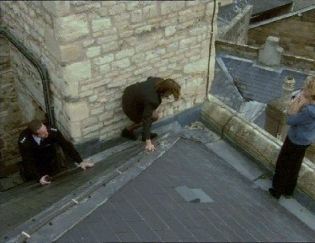 A scene from Bad Girls where Helen Stewart is knelt on a roof trying to talk to Zandra Plackett who is stood by the edge carrying her newborn baby