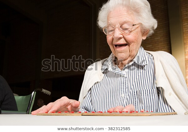 a senior woman with gray hair and a cardigan is DELIGHTED while playing bingo