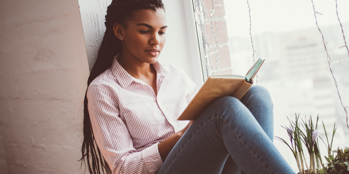 a person with long hair reading in a window