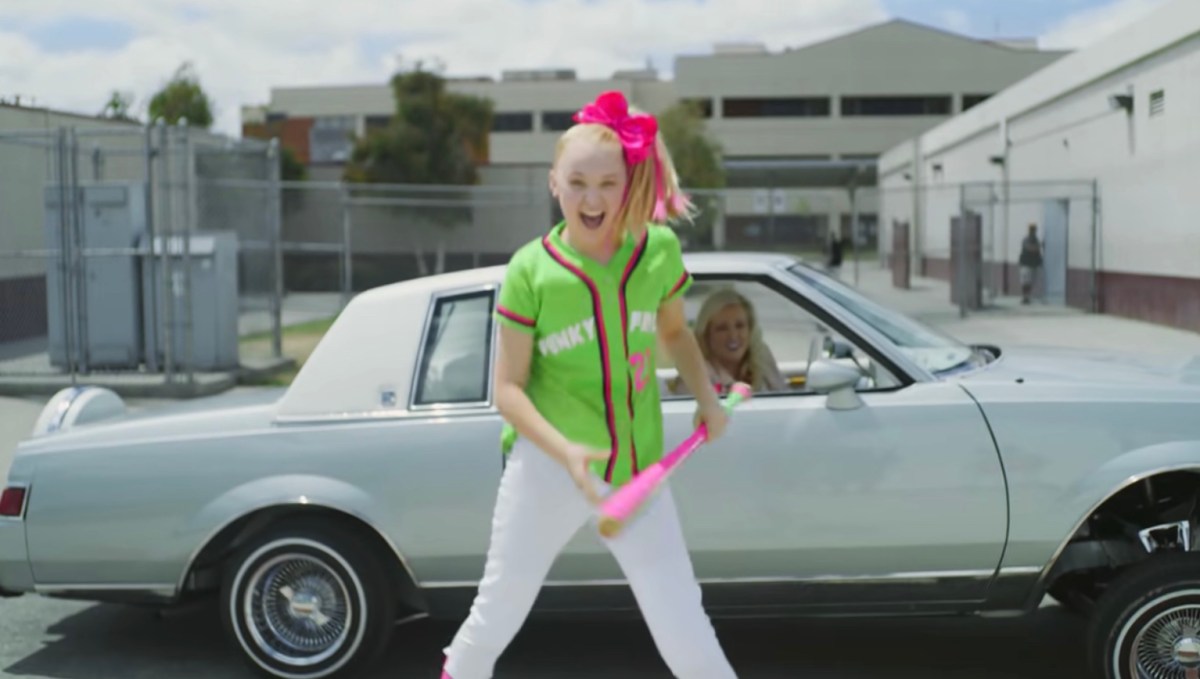 JoJo in a music video wearing a baseball uniform in front of a car