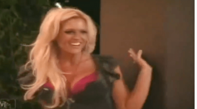 A low-res screenshot of a busty blonde waving