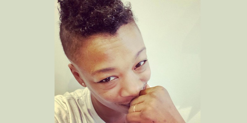 Samira Wiley's face is hidden behind her hand, with her wedding ring glimmering. She has a mohawk, and her eyes are "Smizing" (smiling without smiling) at the camera.