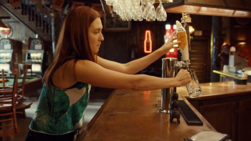 Nicole reaches across the bar to sneak beer from the tap.