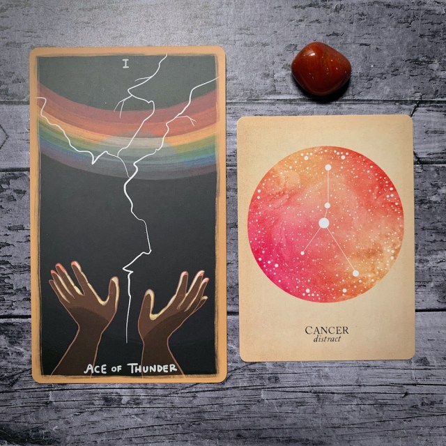 A photo of the tarot card for Ace of Thunder and the astrological card representing Cancer, along with a small crystal