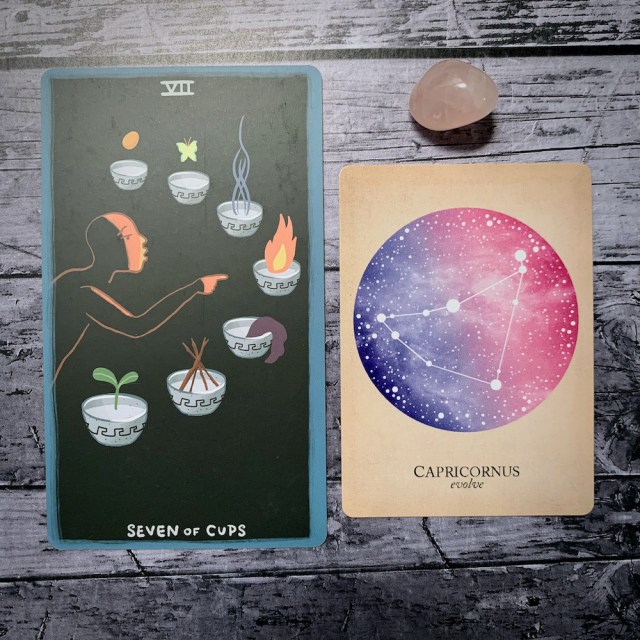 A photo of the tarot card for Seven of Cups and the astrological card representing Capricorn, along with a small crystal