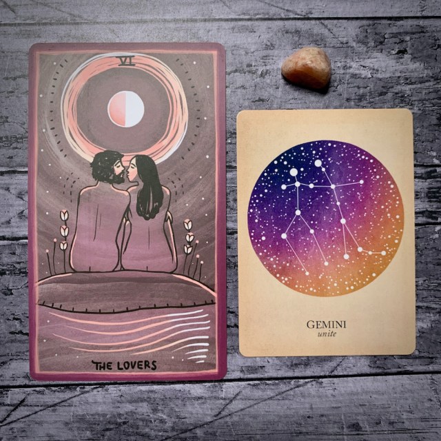 A photo of the tarot card for The Lovers and the astrological card representing Gemini, along with a small crystal