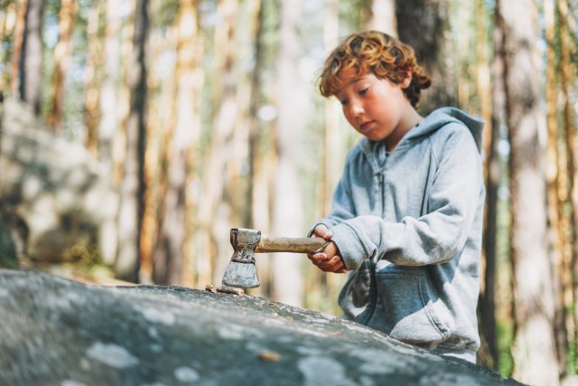 A stock photo of a young boy playing with a hatchet in the woods