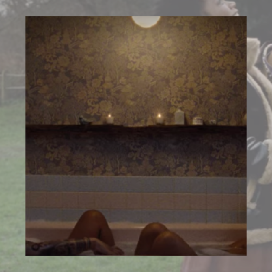 Image shows a photo of two people in a bathtub. You can only see their knees and wallpaper with candles lining the bath.