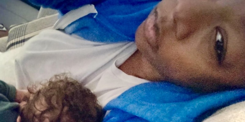 A close up of Samira Wiley looking very tired in a blue hoodie with her newborn daughter, George, in her arms.