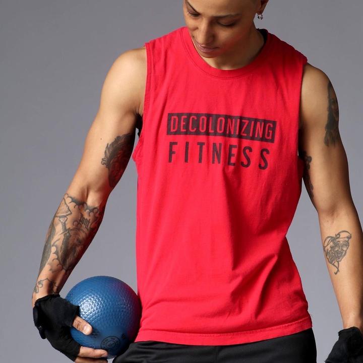 Model wearing red muscle tee that says "Decolonizing Fitness" on it in black lettering