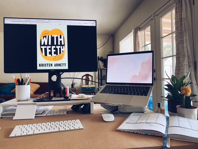 Laneia's desk with her laptop, separate monitor, keyboard, mouse, notebook / calendar / journal situation, a cup of pens and a few plants