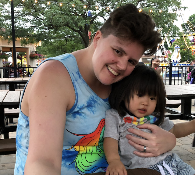 The author's spouse is holding their adorable baby, both wearing rainbow shirts