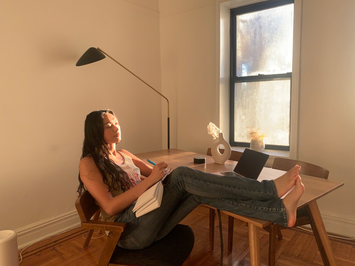 Xoai sitting at her desk writing in her notebook as light streams through the window.