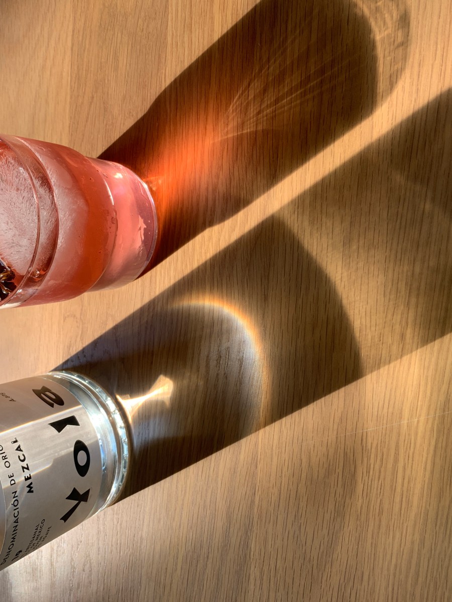 A bottle of mezcal and a cup of coconut water. The light refracted through the bottle creates a rainbow.