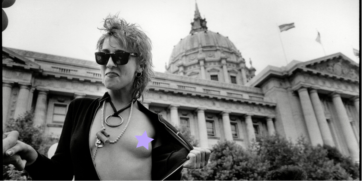 Photo by Bromberger Hoover Photography/Getty Images. The photo is vintage, in black and white, and is of a person, o-ring around their neck, in front of the US capitol building, and pulling back their shirt to reveal an exposed breast. Autostraddle had to cover up the nipple to abide by social media guidelines, so we used a lavender star.