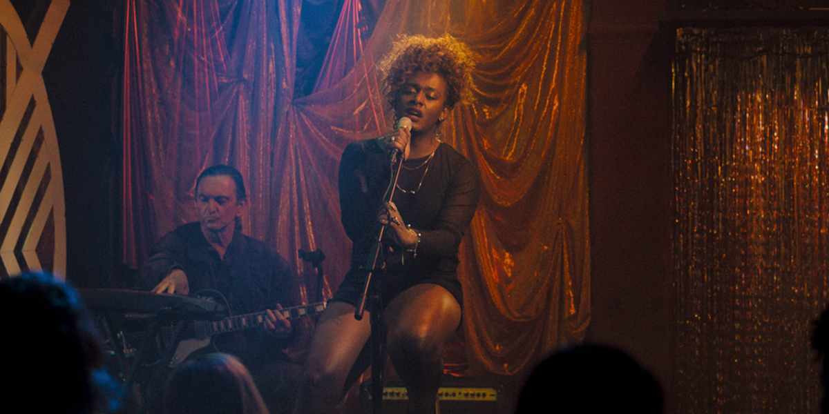 September Mornings: Liniker as Cassandra sings on stage seated wearing a black dress