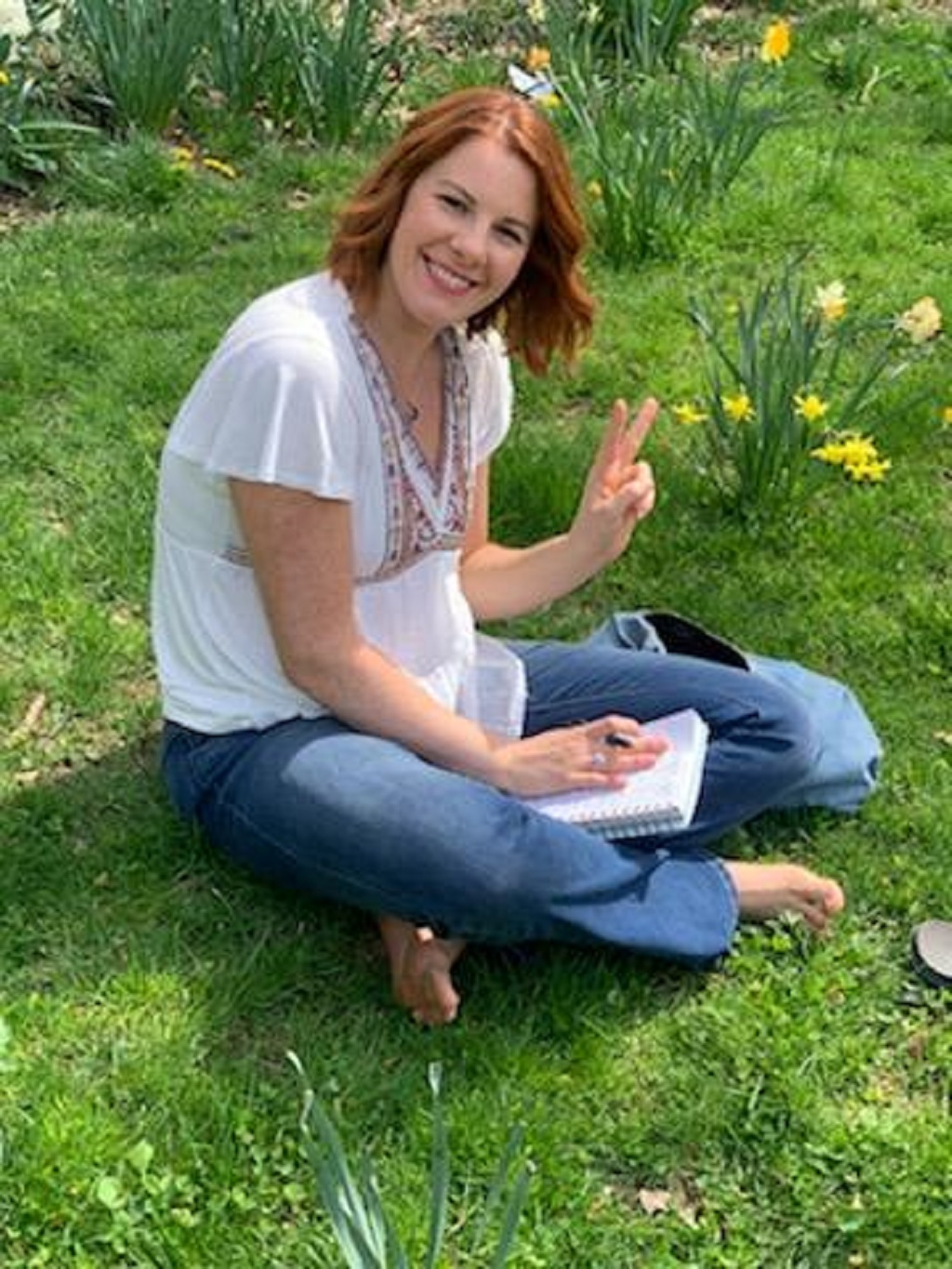 Allison St. Rock sitting cross legged on the grass and making a peace sign