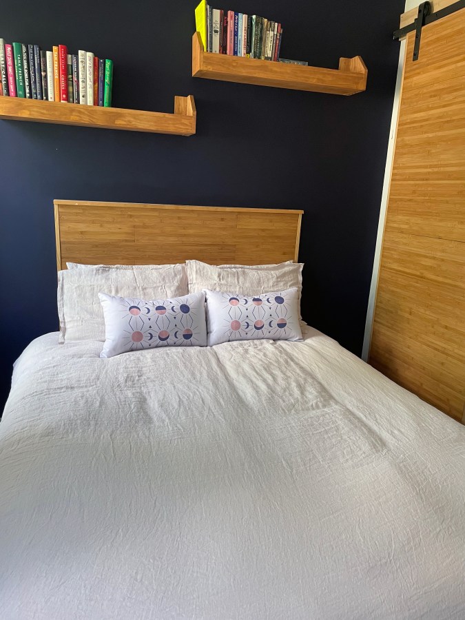 A headboard and matching bookshelves against a dark purple wall, a bed with a light pink duvet in the foreground