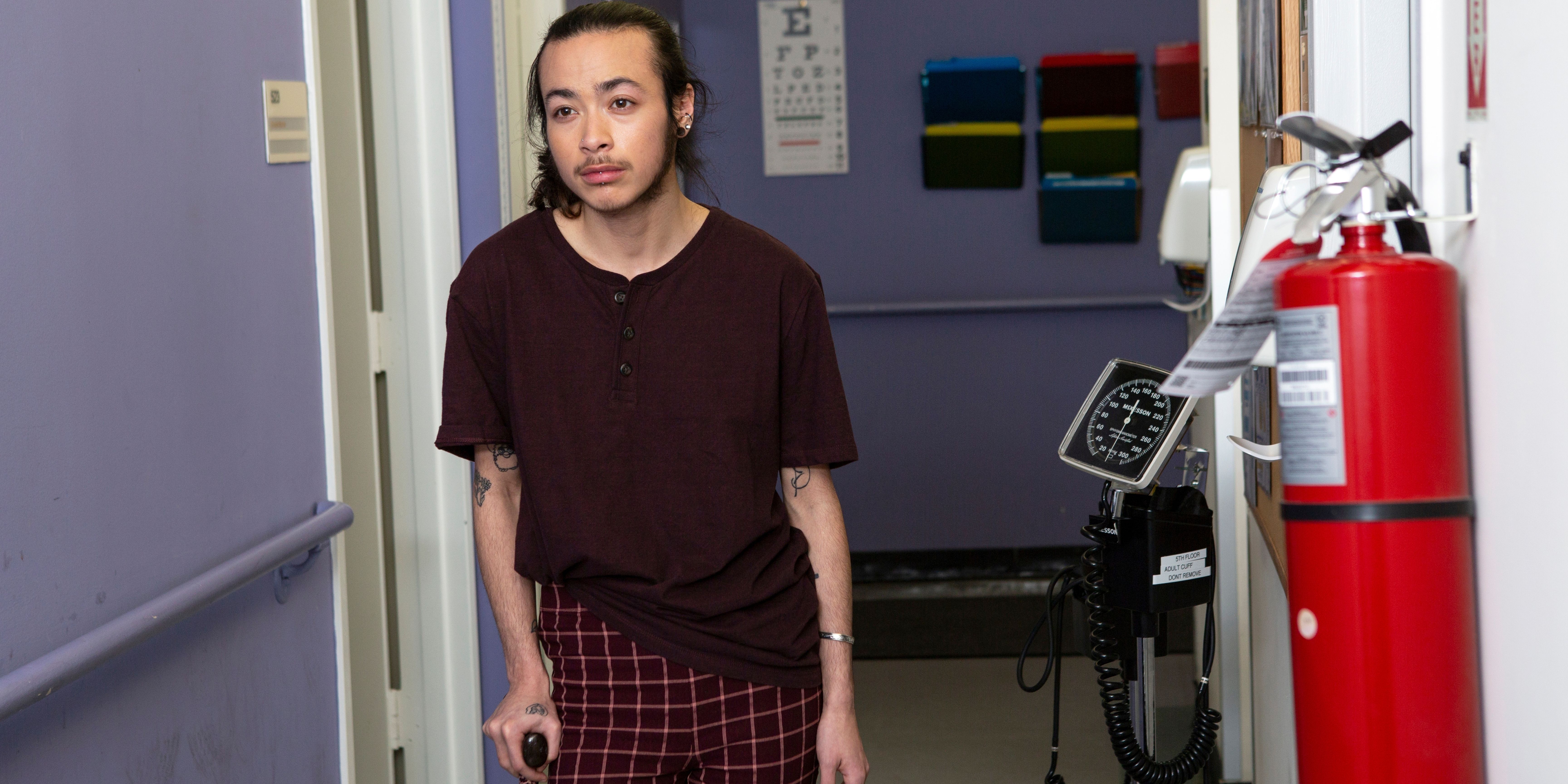 A genderqueer person with a cane walking down the hallway in a h