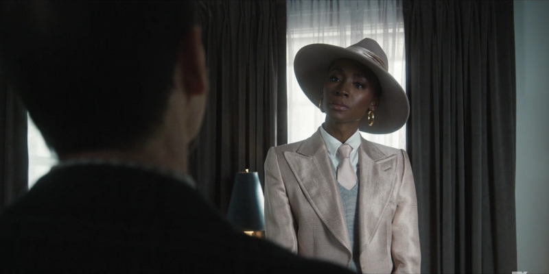 Angelica Ross is wearing a tan three-piece suit and a tan hat.