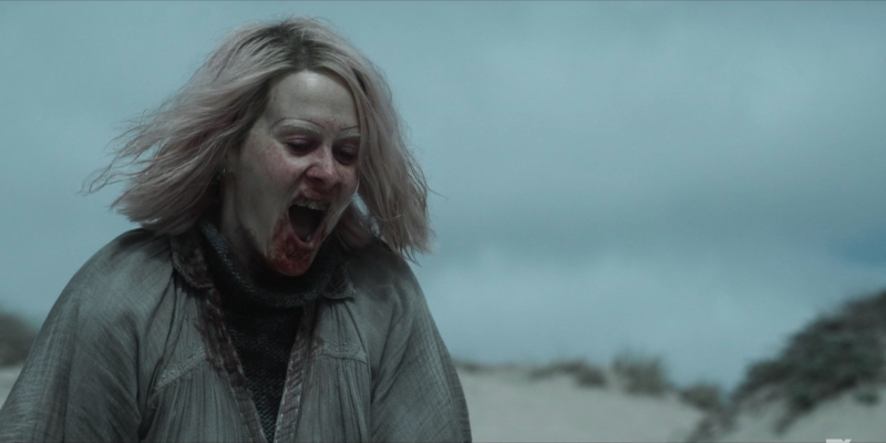 Sarah Paulson as TB Karen stands on the beach with her mouth open covered in blood