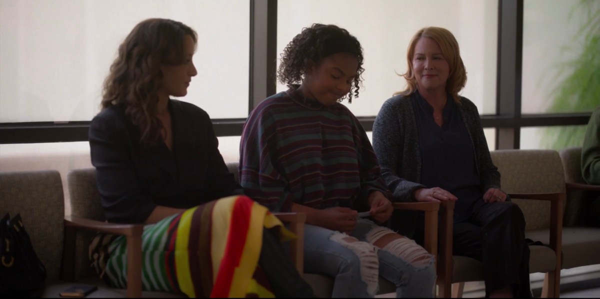 Angie staring at her lap while her Moms stare at her in the hospital waiting room