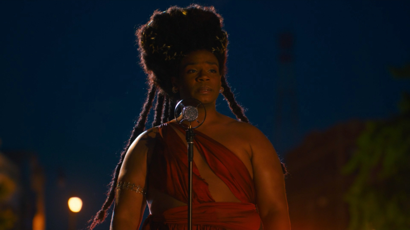 Armand Fields as King standing at a microphone in a dream sequence wearing a red dress