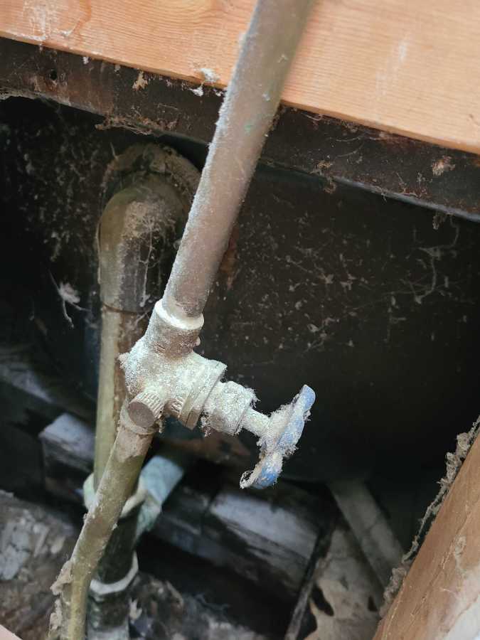 A cobweb covered plumbing access hole leading to a 100+ year old cast iron tub that is inexplicably covered.