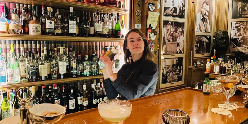 Leisha Hailey is shaking a drink while standing behind a bar