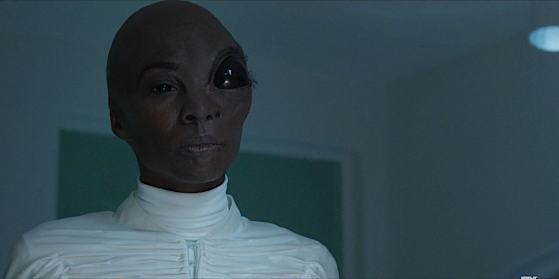 Angelica Ross as a half human half alien. She's wearing a futuristic white robe, has a giant head, and one of her eyes is giant and black.