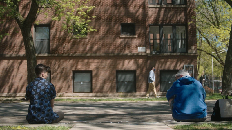 Theo Germain and Abby McEnany sit apart on a curb.