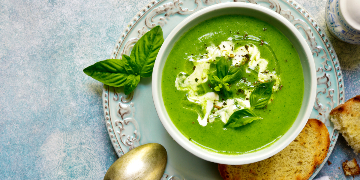 A bowl of green soup with a little sour cream drizzle